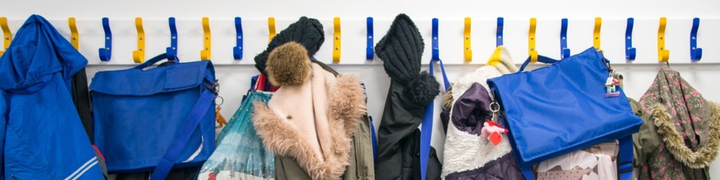 Row of blue and yellow coatpegs with coats and bags hanging from them